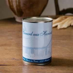 Boîte de canard aux haricots dressée devant des feuilles de maïs séchées