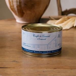 Large boîte de confit de demi-canard, étiquette illustrée d’une ferme, sur une table