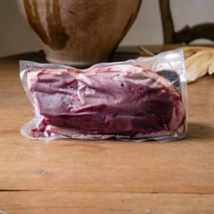 Magret de canard frais sous vide, peau claire et chair rouge sombre, sur le bois