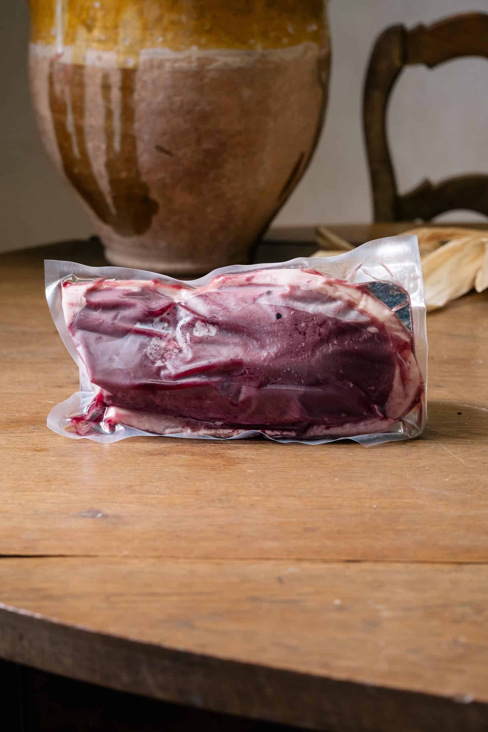 Magret de canard frais sous vide, peau claire et chair rouge sombre, sur le bois