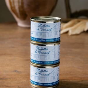 Trois boîtes de rillettes de canard empilées sur une table en bois