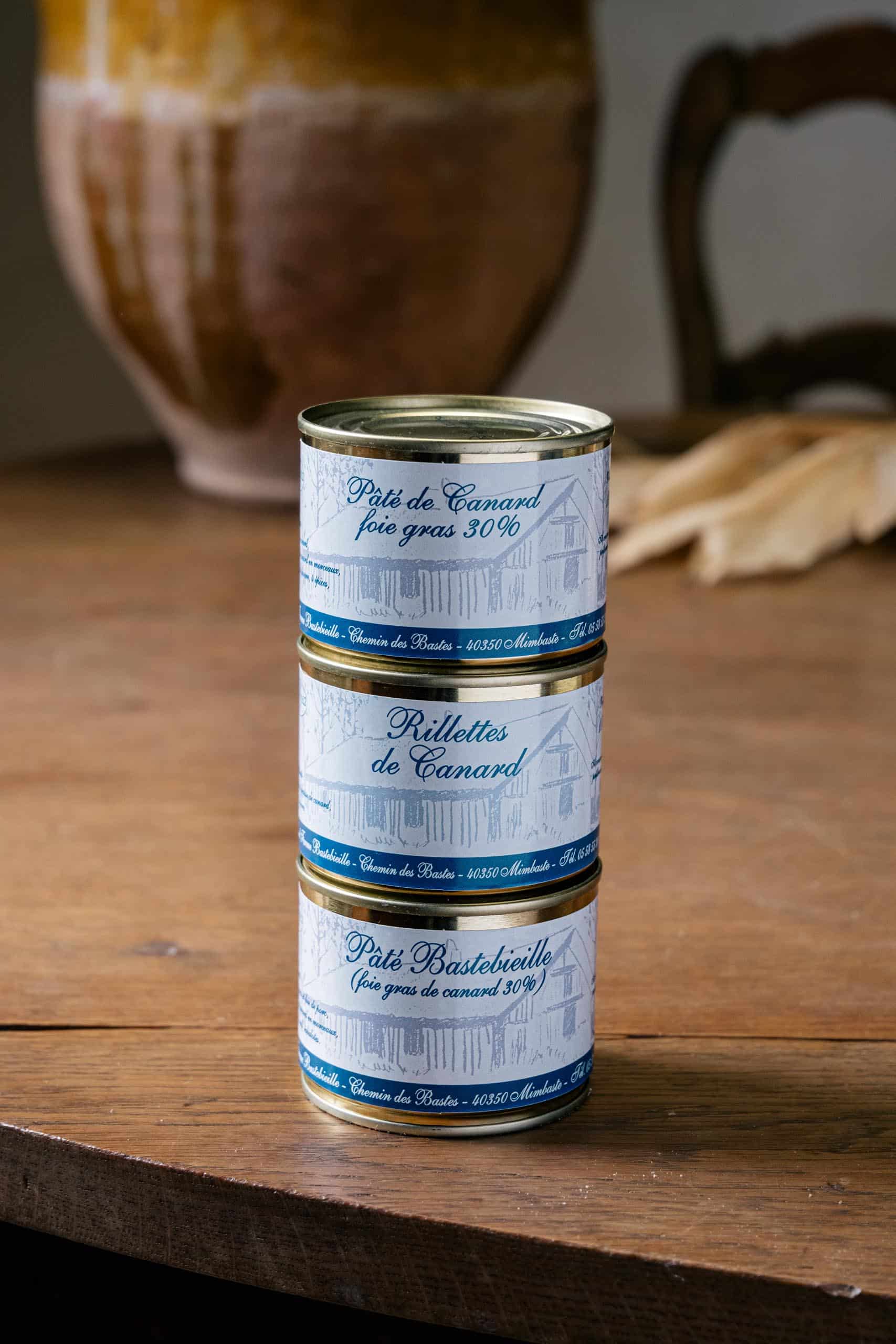 Pile de trois boîtes, pâté de canard, rillettes et pâté Bastebieille, devant la jarre
